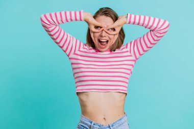 Komik, şakacı, genç bir kadın aptalca yüz ifadeleri takınıyor, suratını buruşturuyor, etrafta takılıyor, dil gösteriyor, aptalca bir ifade sergiliyor. Mavinin üstündeki güzel kız mavi stüdyoda tek başına.