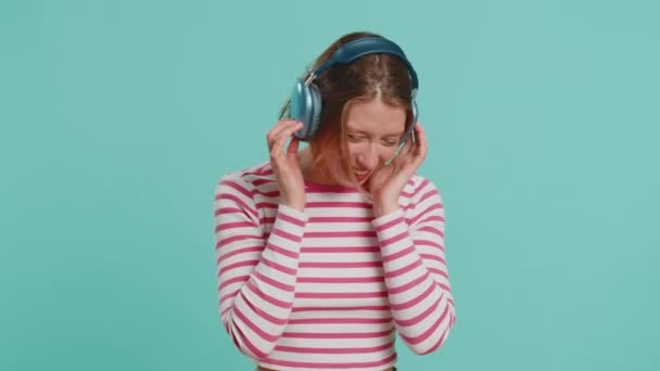 戴着耳机的快乐女人 一边听着音乐 一边跳着迪斯科 在派对上放松自己 戴着太阳镜的漂亮女孩被隔离在工作室的蓝色背景中 — 图库视频影像