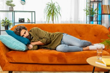 Orta Doğu 'lu yorgun bir adam yatakta uzanıyor ve evde dinleniyor. Kaygısız genç sakallı adam uyukluyor, rahat koltukta yastıklarla uyuyakalıyor. Kapalı gözler, tek başına gündüz uykusunun tadını çıkar.