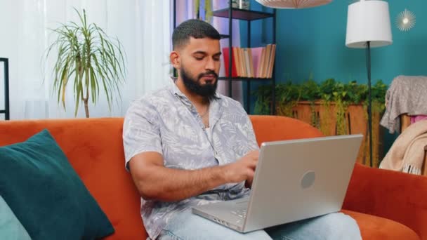 印度男子在客厅完成工作后坐在沙发上关闭笔记本电脑 年轻的阿拉伯裔自由职业者在网上工作 在家里的沙发上做远程工作 电子学习 在笔记本电脑上浏览互联网 — 图库视频影像