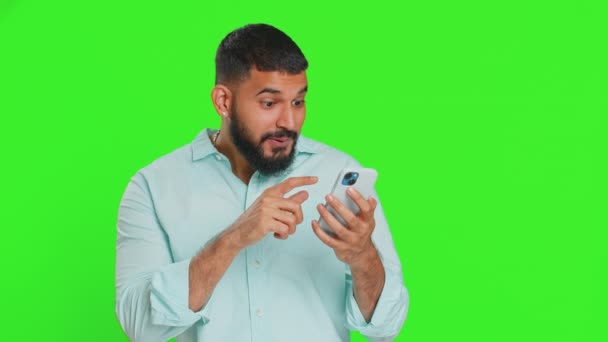 Szczęśliwy Podekscytowany Indyjski Młody Człowiek Facet Używać Smartfona Wpisując Maszynie — Wideo stockowe
