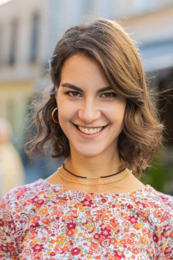 Mutlu güzel bir genç kadının portresi. Dostça gülümseyen, kameraya bakan mutlu yüz ifadesi. Hayal kuran, dinlenen, rahatlayan, dışarıda iyi haberler veren. Şehirdeki sokak geçmişi olan bir kız. Dikey