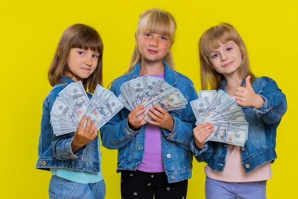Rich happy teenage girls waving money dollar cash banknotes bills like a fan, success business career, lottery game winner, big income, wealth, donation. Little children sisters. Three siblings kids