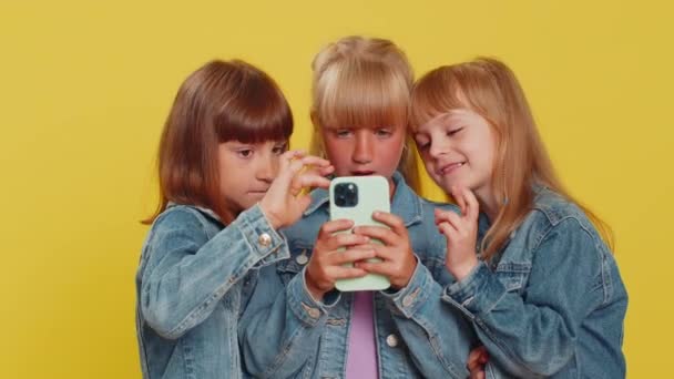 ティーンエイジャーの女の子は モバイルスマートフォンタイピングブラウジングを使用して Wow Yesは偉大な大きな勝利を見つけました 良いニュースお祝い オンラインゲームをプレイ 小さな子供たち 黄色の背景にある3人の兄弟姉妹 — ストック動画
