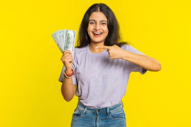 Zengin, mutlu, Hintli genç bir kadın hayranı, başarılı bir iş adamı, piyango talihlisi, büyük gelir getiren banknotlar sallıyor. Sarı arka planda izole edilmiş Arap Hindu kız