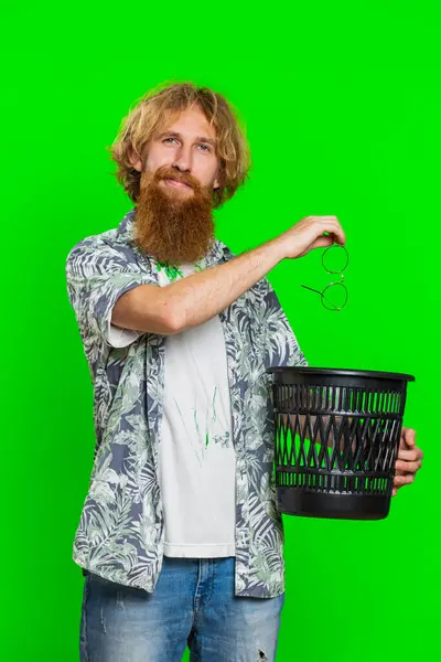 Redhead man taking off throwing out glasses into bin after medical vision laser treatment therapy surgery looking smiling at camera, heal, cure. Handsome guy isolated on green chroma key background
