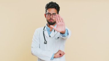 Dur, yeter. Ciddi Hintli genç doktor kardiyolog hayır dedi. Bitiş uyarısı, erişimi yasaklayan jest, iletişimi kesme. Arap eczacı, bej arka planda izole edilmiş.