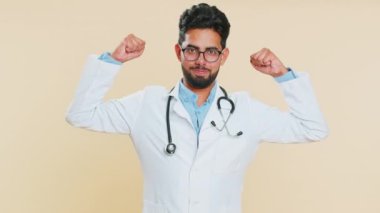 Güçlüyüm. Hintli genç doktor kardiyolog pazılarını gösteriyor ve başarılı olmak için hak enerjisi için savaşma gücü arıyor. Bej arka planda Arap eczacı.