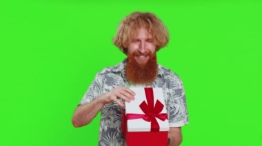 Mutlu Kafkasyalı adam kırmızı kurdeleli doğum günü hediyesi kutusunu açıyor. Tatil sürprizi konsepti. Gülümseyen kızıl sakallı adam yeşil krom anahtar arka planda izole edilmiş harika bir hediye aldı.