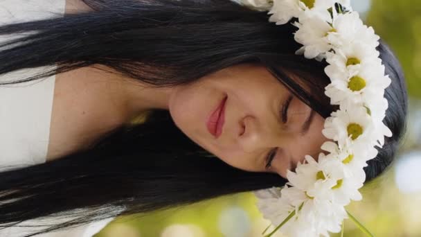 カメラでフレンドリーに見える野生のデイジーの花の花の花の花輪で笑顔のコーカサス中年の女性の肖像画 リラクゼーションは屋外で満足しています 森林公園の背景にある健康的な女性 — ストック動画
