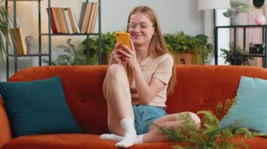 Kanepede oturan kadının portresi evde gülümseyen bir cep telefonu kullanıyor. Akıllı telefon sosyal medya uygulamaları üzerinden rahatlama filmi izlerken mesajları paylaşan genç kız