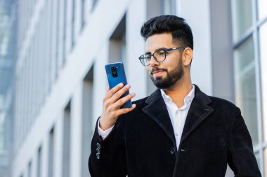 Akıllı telefon kullanan yakışıklı Hintli işadamı mesajları cevaplıyor açık havada mobil ekran uygulaması gibi internette sohbet ediyor. Şehir merkezindeki Hindu serbest çalışan Arap bir adam. İş adamları