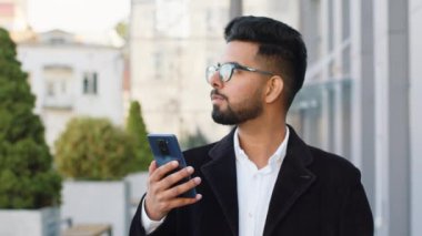Akıllı telefon kullanan yakışıklı Hintli işadamı mesajları cevaplıyor açık havada mobil ekran uygulaması gibi internette sohbet ediyor. Şehir merkezindeki Hindu serbest çalışan Arap bir adam. İş adamları