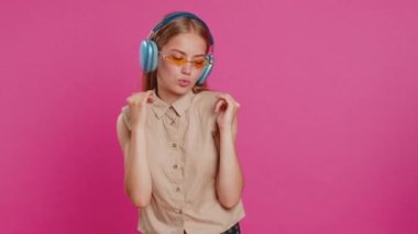 Kulaklık takmış, müzik dinleyen, dans eden, eğlenen, el kol hareketi yapan, partide gevşeyen mutlu bir kadın. Güneş gözlüklü sarışın kız stüdyo pembe arka planda izole edilmiş.