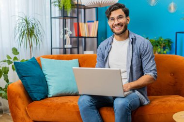 Oturma odasındaki dizüstü bilgisayar işini bitirdikten sonra koltukta oturan Hintli adam. Genç Arap serbest çalışan adam evdeki kanepede uzaktan kumanda işinde çalışıyor. Defter bilgisayarında e-öğrenme, internette gezinme
