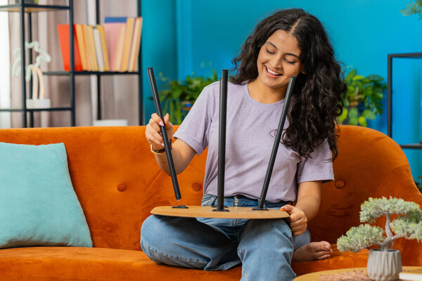 Happy Indian woman finishing assembling furniture at home. Successful table desk collect, repair fixing. Arabian girl after moving into new apartment. Advertisement of a furniture store. Mortgage