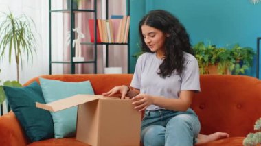 Paketleri açan mutlu Hintli genç kadın evde oturuyor. Gülümseyen Arap Hindu kız alışveriş sitesi müşterisi karton kutu açarken hızlı posta yoluyla hediye alıyor.