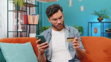 Hintli adam parayı transfer ederken kredi kartı ve akıllı telefon kullanıyor. Ev içinde alışveriş yaparken nakit para almıyor. Mutlu Arap adam kanepede oturuyor.