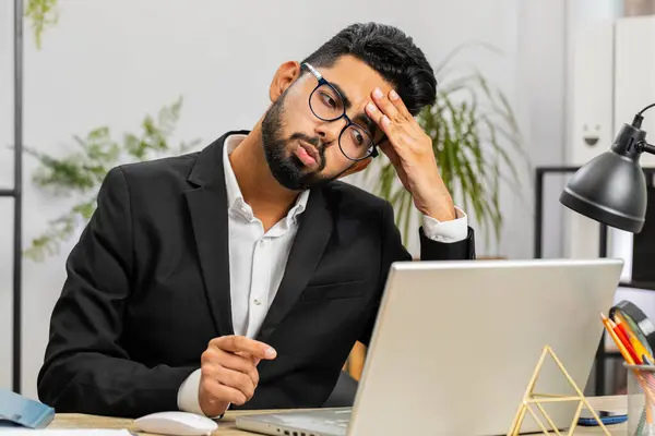 Irritated tired Indian business man while working on laptop, unexpected online website problem, computer virus data loss by hacking. Freelancer feeling mad about broken notebook at office workplace