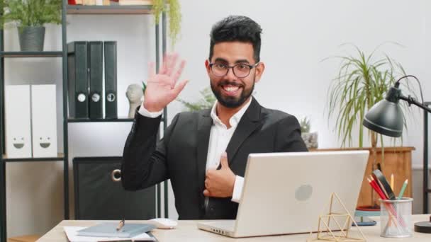 你好Hello 在笔记本电脑上工作的印度商人面带微笑 对着相机友好地微笑 挥挥手表示问候 问候或告别 热情好客地在家里办公室的办公桌前迎接 — 图库视频影像