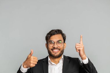 Hintli işadamı başparmaklarını havaya kaldırarak boş bir yeri işaret ediyor. Ticari metin fotokopi alanı reklamı için reklam alanı. Gri arka planda izole adam