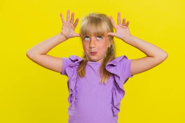 Neşeli, komik, genç, sevimli kız kameraya surat asıyor, şakalaşıyor, aptal suratıyla maymun taklidi yapıyor, alay ediyor. Sarı arka planda sarışın çocuk. Küçük çocuklar