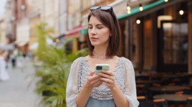 Akıllı telefon kullanarak gülümseyen genç bir kadın. Kısa mesajlar yazarak interneti tarıyor, işi bitiriyor, dışarıdaki kameralara bakıyor. Şehir caddesinde yürüyen bir kız turist. Kasaba yaşam tarzları