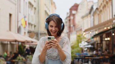 Kablosuz kulaklıklar takmış, açık havada dans eden ve en sevilen disko rock 'n roll müziğini dinleyen mutlu, gevşemiş genç kadın. Kentsel Avrupa şehir sokaklarında yürüyen bir kız