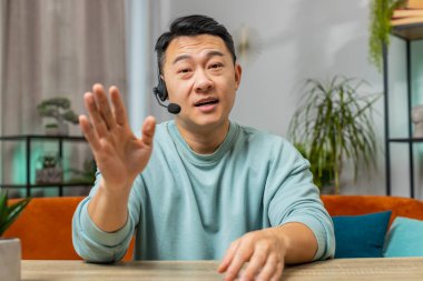 Kulaklık takan Asyalı Çinli adam, serbest çalışan çağrı merkezi ya da destek operatörü yardım hattı. Çinli bir adam müşterisiyle ya da iş arkadaşıyla konuşuyor. Evde tek başına el sallıyor.
