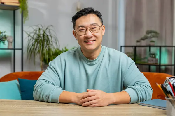 Portrait of happy calm Asian man at home smiling friendly, glad expression looking at camera dreaming resting relaxation feel satisfied good news celebrate win. Chinese middle-aged guy in living room