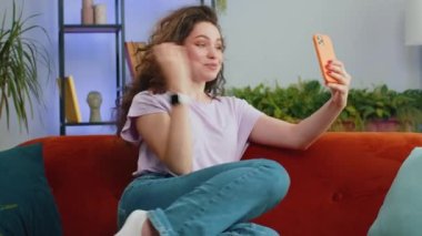 Kanepede oturan arkadaşlarıyla telefon konuşması yapan genç bir kadının portresi. Mobil akıllı telefon hoparlörlerinden hoşlanan mutlu bir kız modern ev oturma odasında içeride konuşuyor.