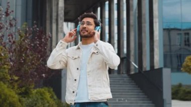Kablosuz kulaklıklı mutlu, rahat Hintli adam dans ediyor, açık havada dans eden enerjik disko müziği dinliyor. Şehir merkezindeki caddede duran Arap Hindu neşeli adam. İş adamları