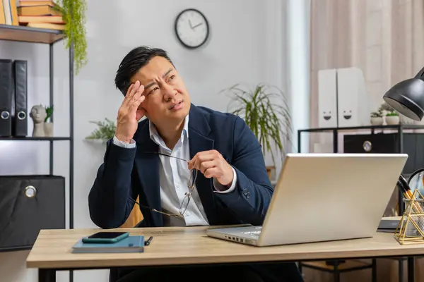 Tired Asian businessman feeling worried about financial problem, stress at home office workplace. Chinese freelancer broker man frustrated thinking of money debt, budget loss, bankruptcy. Overworking