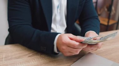 Zengin işadamlarının yakın çekimleri. 100 dolar nakit para sayıyorlar. Ev ofis çalışma masasında dizüstü bilgisayar kullanıyorlar. Profesyonel serbest çalışan mutlu bir adam. Kazanç, başarı sözleşmesi, kazanç.
