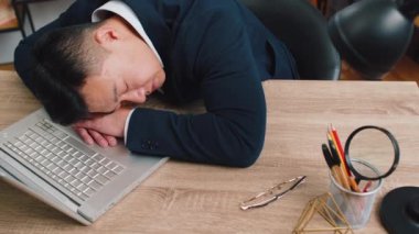 Sıkıcı Asyalı iş adamı dizüstü bilgisayarda çalışıyor, ofis masasında el ele uyuya kalıyor. Yorgun, serbest çalışan, orta yaşlı, işkolik bir adam. İstihdam, meslek, işsiz