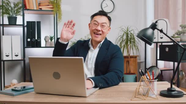 你好Hello 在笔记本电脑上工作的亚洲商人面带微笑 对着相机友好地微笑 挥挥手表示问候 问候或告别 热情洋溢地在总部办公室的办公桌前迎接 — 图库视频影像