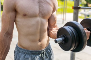Yakın plan atletik üstsüz kaslı adam kol ağırlığı kaldırıyor halter egzersizleri yapıyor, kol kaslarını şişiriyor. Çocuk parkındaki adam. Spor fitness rutini, vücut geliştirme çalışması. Kuvvet motivasyonu