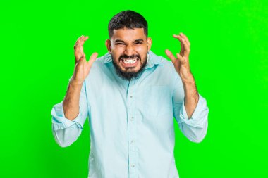 Gerginlikten bağıran sinirli Hintli adam korku, umutsuzluk, şaşkınlık şokun öfkesini ve kavgasını hisseder. Yeşil krom anahtar arka planda izole Arap genç adam