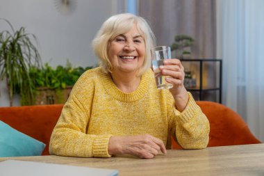 Susamış son sınıf öğrencisi kadın susuzluğunu gidermek için bir bardak filtreli su içiyor. Ters osmoz filtresinden sonra su. İyi yaşam sabah alışkanlıkları olan büyükanne sağlıklı yaşam tarzları var.