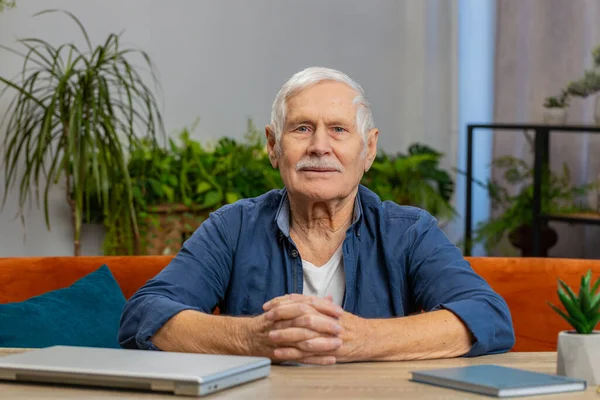 Portrait of happy calm senior old man smiling glad expression looking dreaming resting relaxation feel satisfied concept good news celebrate win at home indoor. Elderly mature grandfather sit at table