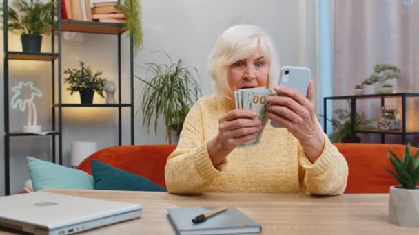 规划家庭预算 笑着数钱的老年妇女用智能手机计算家里的账单 老祖母对收入感到满意 并为计划中的度假礼物存钱 — 图库视频影像
