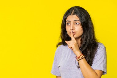 Sessiz olun lütfen. Hintli genç kadın işaret parmağını dudaklarına bastırıyor sessiz jest işareti yapıyor. Sırları söyleme, dedikoduları kes, özel hayatı gizli tut. Sarı arka planda izole edilmiş Arap kız