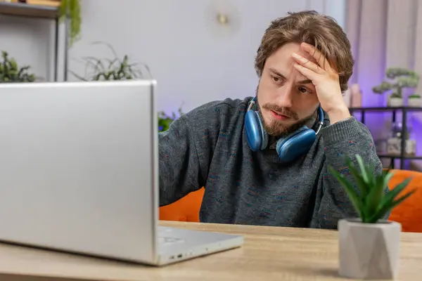 Displeased sad man use laptop notebook typing browsing working loses becoming surprised sudden lottery results bad news fortune loss game fail computer virus crisis. Caucasian guy at home office table