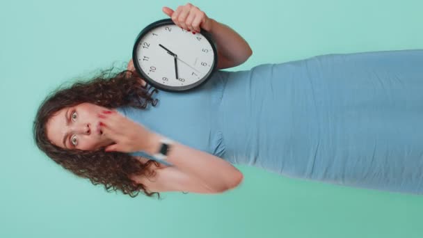 不安を抱える女性は 時計をチェックし 遅くまで仕事をし 遅刻期限を設けています 青いスタジオの背景で時間 時間的に隔離されることを心配する忙しい少女 バーティカル — ストック動画