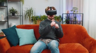 Sakallı adam sanal gerçeklik teknolojisi VR uygulama kulaklığı kullanarak 3D 360 çevrimiçi video oyunu simülasyonu yapıyor ve modern ev dairesinde film izliyor. Gözlüklü adam kanepede oturuyor.