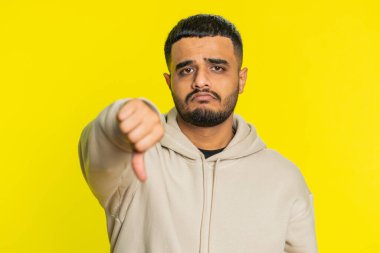 Hoşlanmamak. Mutsuz Hintli adam, hoşnutsuzluğunu, memnuniyetsizliğini ve olumsuz tepkilerini belirterek işaret gösteriyor. Çekici Hindu adam sarı arka planda kapalı yerde izole edilmiş.