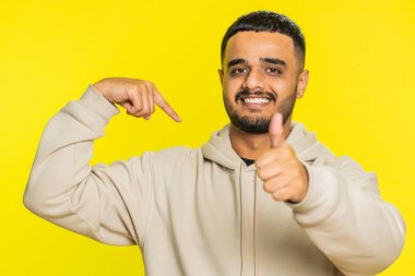 Ben en iyisiyim, beni seç. Heyecanlı genç Hintli adam kendini göstermekten gurur duyuyor, kendine güveni tam, başarıdan çok memnun görünüyor. Arap Hindu adam stüdyo sarı arka planda tek başına izole edilmiş.