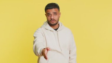 Kameraya uzanan dost canlısı Hintli genç adam, el sıkışma teklif ediyor, nazik bir gülümseme, davetiye, dayanışma ve güven göstergesi olarak karşılıyor. Sarı arka planda izole edilmiş Arap adam.