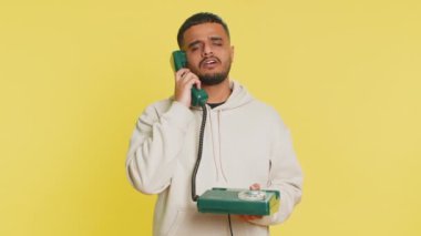 80 'lerin telli vintage telefonundan konuşan sıkılmış Hintli adam sıkıcı hikayelerden bıkmış aptal suratlar yapıyor, iletişim konuşmalarıyla ilgilenmiyor. Sarı arka planda izole edilmiş Arap adam.