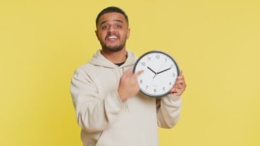 Senin sıran, acele et. Hintli genç adam duvar ofis saati gösteriyor, tamam, başparmağınla kamerayı, reklamı, son teslim tarihini göster. Stüdyo sarı arka planda izole edilmiş Arap bir adam.